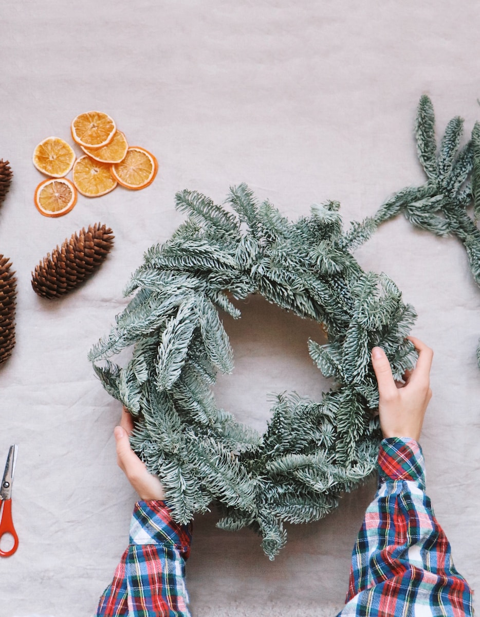 a person making a wreath with pine cones and oranges